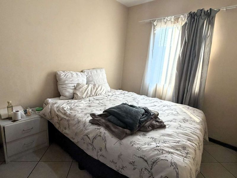 A functional bedroom featuring tiled flooring and natural light through a window with installed curtain rods.