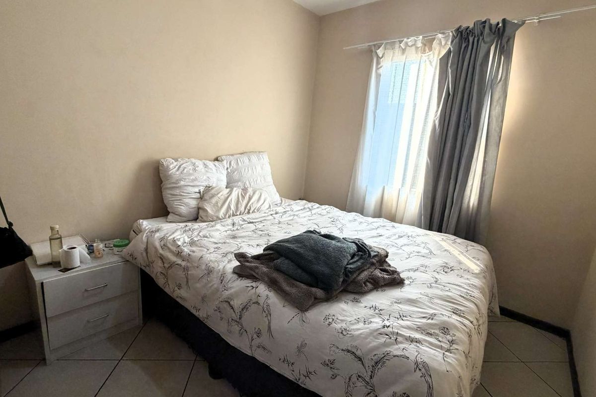 A functional bedroom featuring tiled flooring and natural light through a window with installed curtain rods.