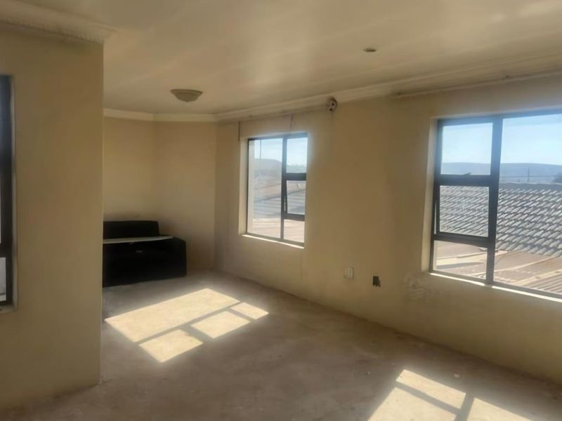 An empty living room featuring aluminium window frames, coved cornicing, and recessed lighting, awaiting final flooring and wall finishes.