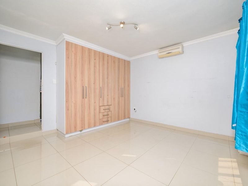 A bright, empty bedroom featuring light-colored tiled flooring, built-in wooden cupboards, and a wall-mounted air conditioning unit.
