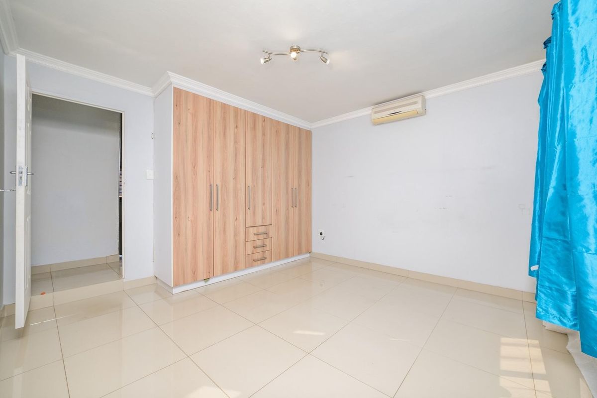 A bright, empty bedroom featuring light-colored tiled flooring, built-in wooden cupboards, and a wall-mounted air conditioning unit.