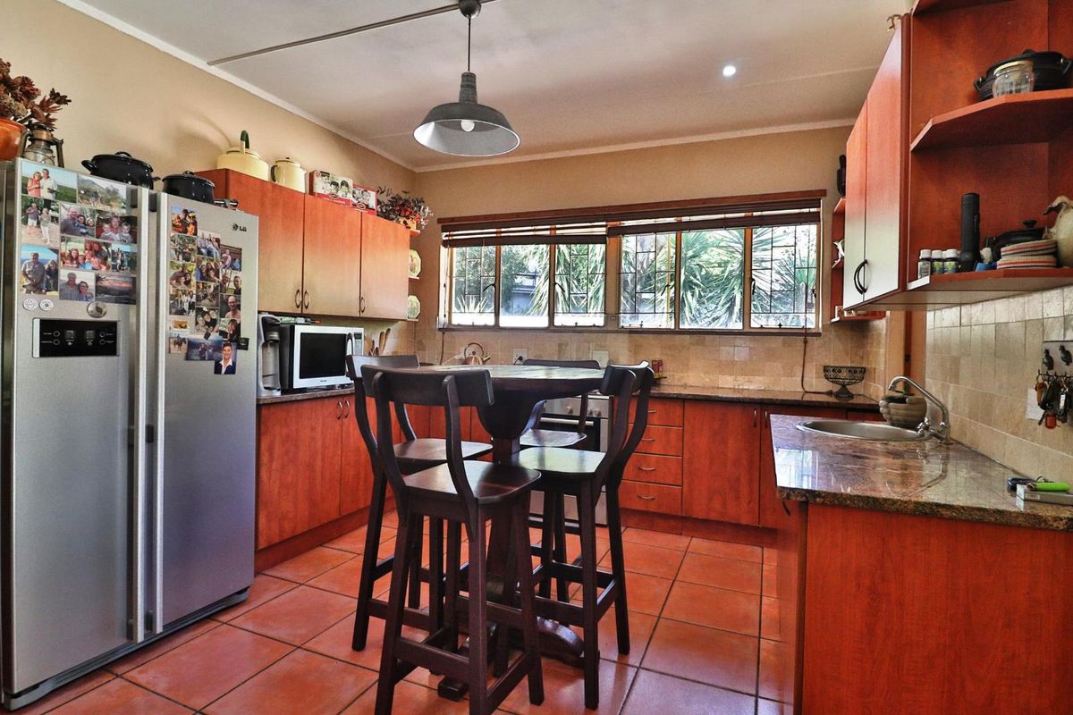 A functional kitchen featuring warm-toned wooden cabinetry, granite countertops, tiled flooring, and a central breakfast nook area with natural light.