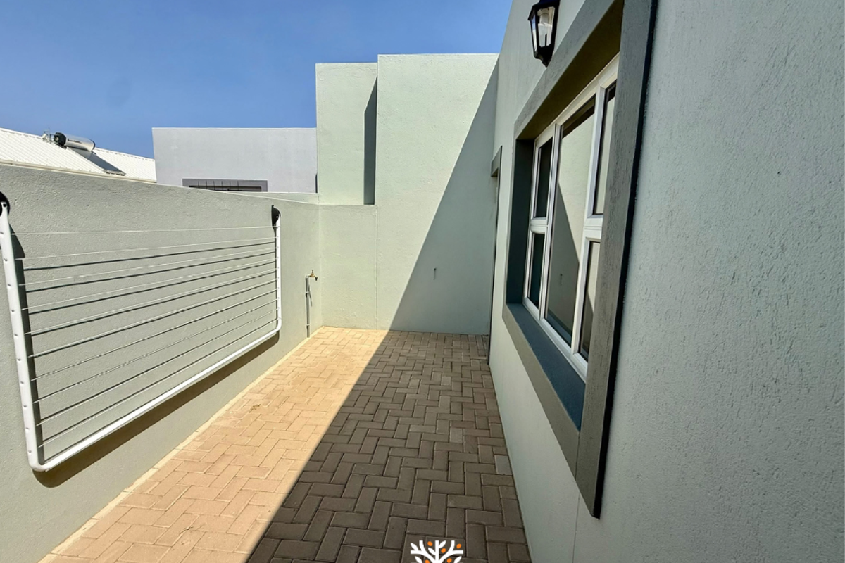 A clean, paved rear courtyard area featuring a wall-mounted drying rack, external water tap, and modern exterior wall lighting.