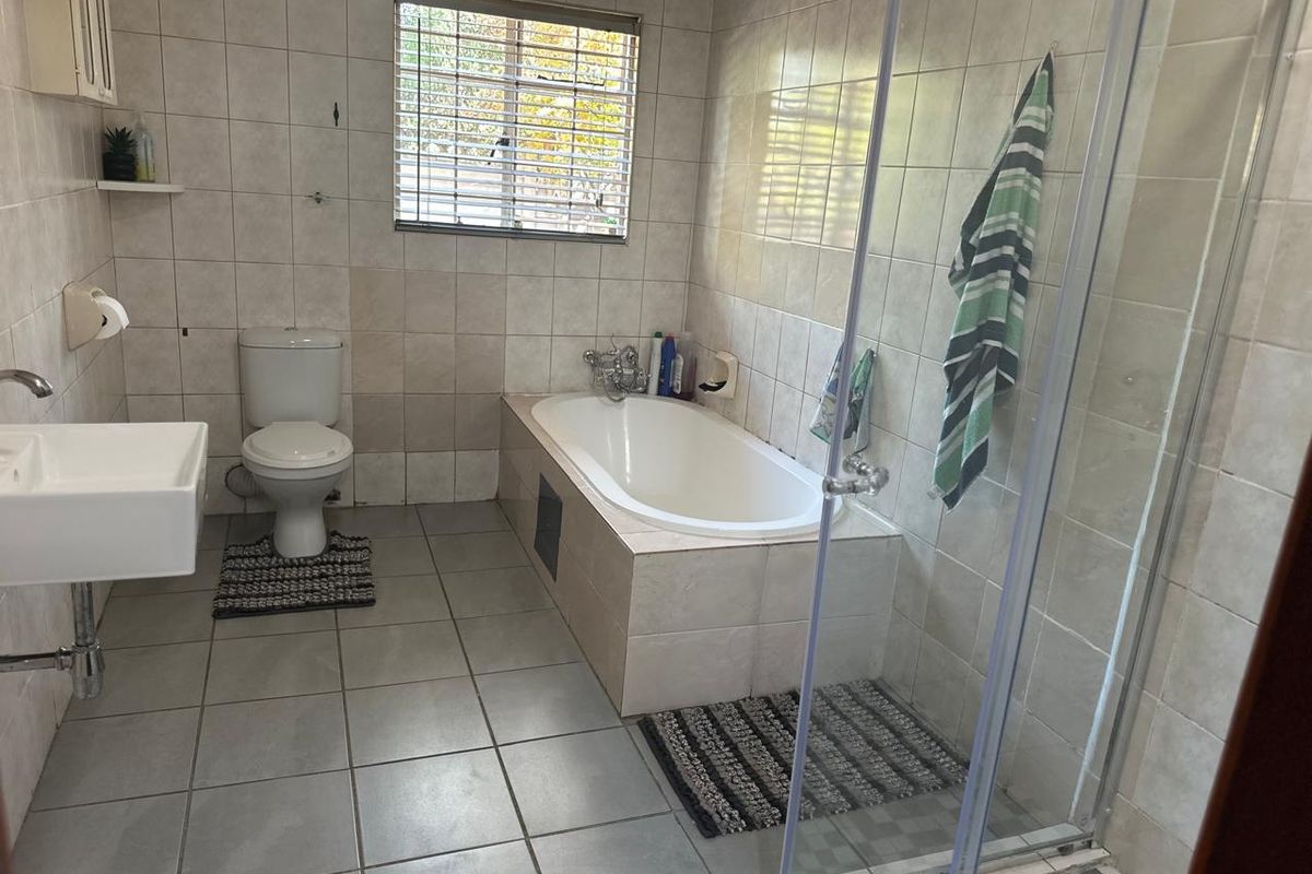 A functional bathroom featuring a built-in bathtub, a separate glass-enclosed shower, a wall-mounted basin, and neutral floor-to-ceiling wall tiling.