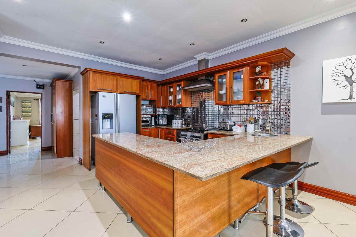 A well-appointed kitchen featuring warm wooden cabinetry, granite countertops, a gas hob with extractor fan, and a stylish mosaic tile backsplash.