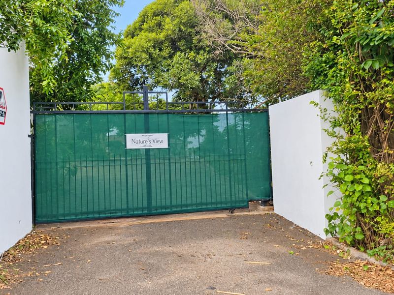 Front entrance view of the property featuring a sliding security gate, boundary walls, and paved driveway access.