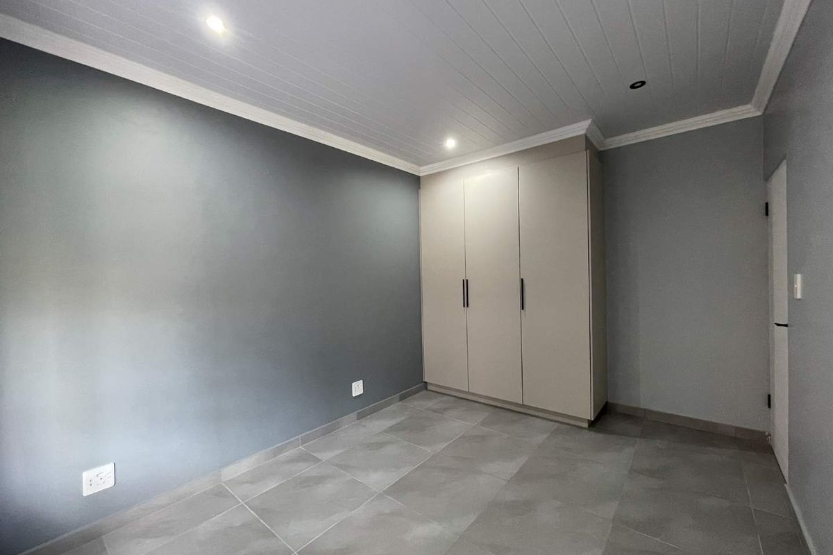 A clean, empty bedroom featuring modern grey tiled floors, built-in cupboards, and a white tongue and groove ceiling with recessed lighting.