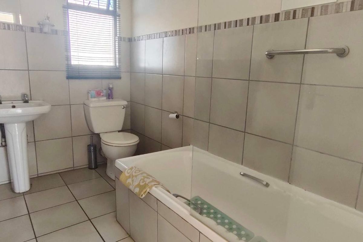 A functional bathroom featuring a pedestal basin, toilet, and a bathtub with a glass shower screen, finished with neutral wall and floor tiles.