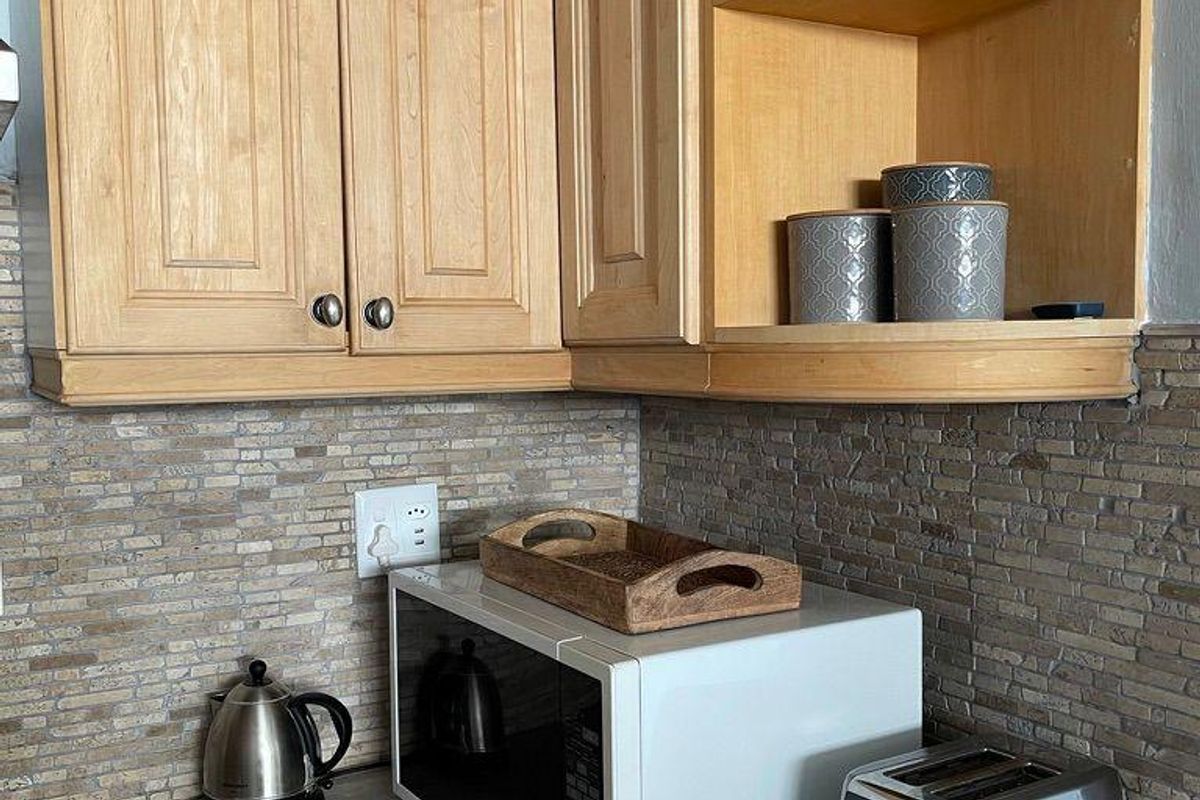 A kitchen corner featuring light timber cabinetry, a stone-look laminate countertop, and a textured stacked stone backsplash.