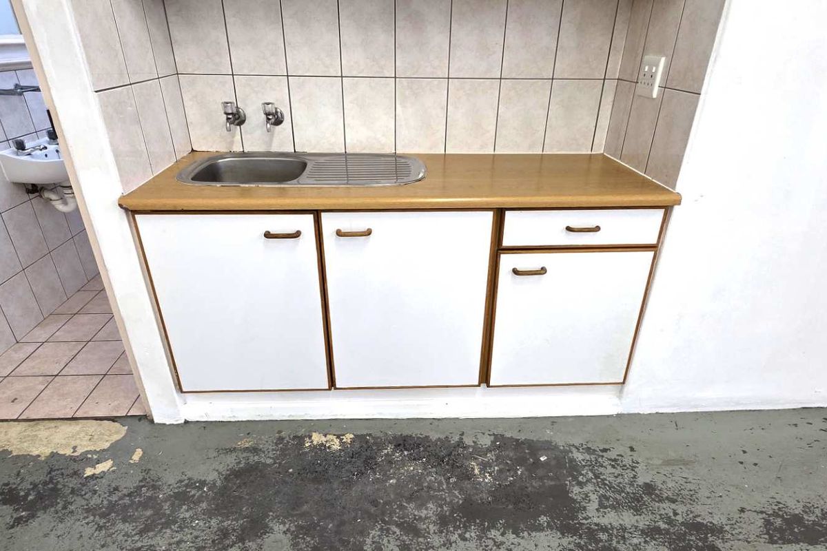 A functional kitchenette area featuring built-in cabinetry, a stainless steel sink, and tiled splashbacks, adjacent to a small tiled washroom area.