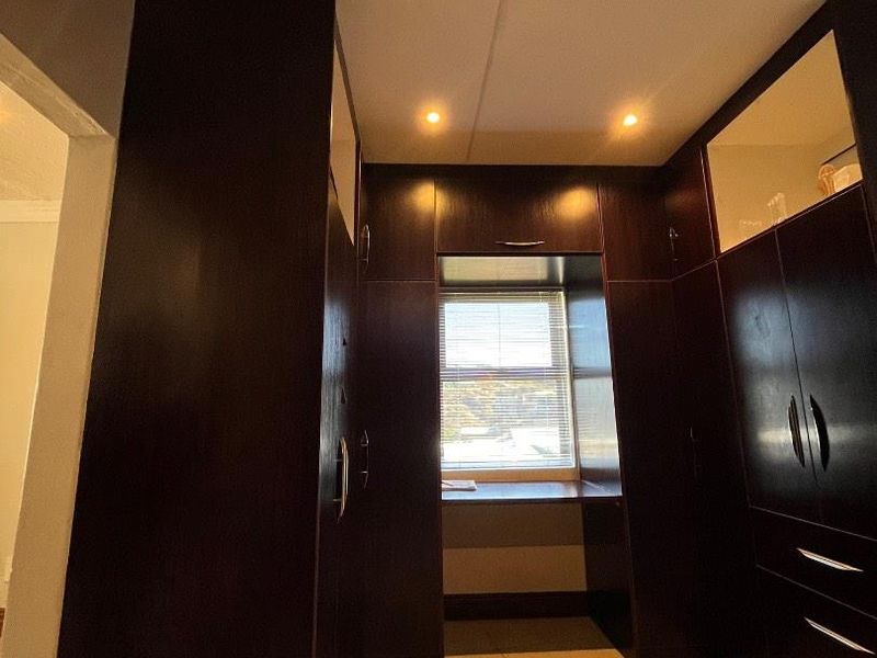 A spacious bedroom featuring extensive dark wood built-in cabinetry, tiled flooring, and a dedicated desk area integrated into the window alcove.