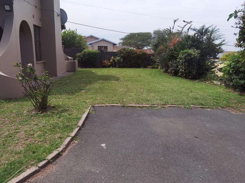 A view of the rear garden featuring a well-maintained lawn, asphalt driveway area, and established boundary landscaping.