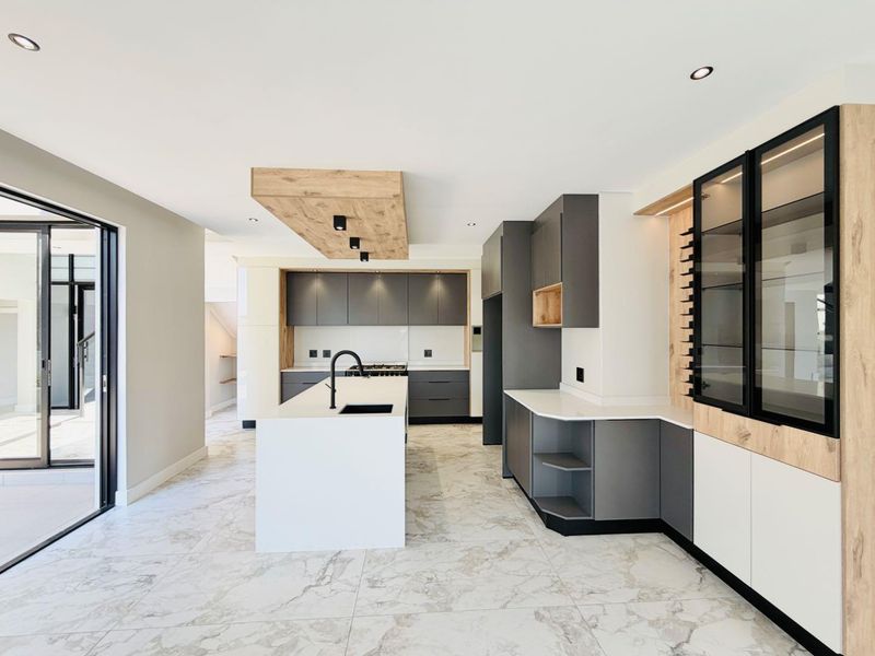 Modern, high-end kitchen featuring a central island, sleek grey and wood-tone cabinetry, quartz countertops, and premium marble-look flooring with direct access to the patio.