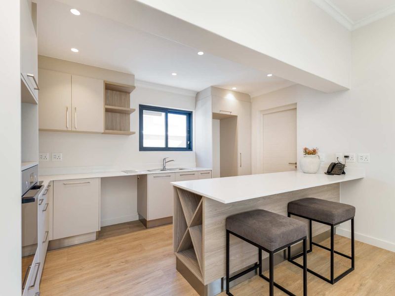 Modern kitchen featuring sleek cabinetry, stone countertops, a breakfast bar, and integrated oven, finished with high-quality laminate flooring and recessed lighting.