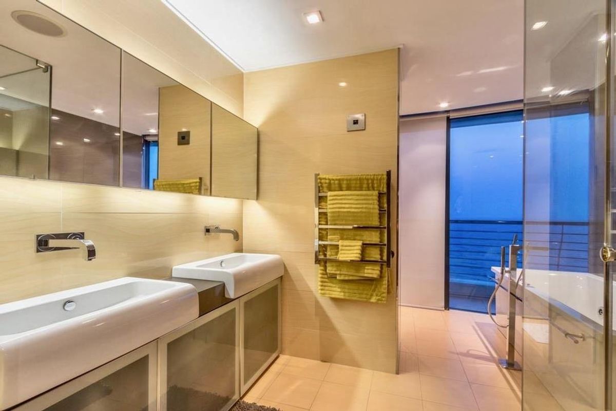 Modern penthouse bathroom featuring a double vanity with integrated sinks, wall-mounted faucets, large mirrored cabinetry, and a separate glass-enclosed bathtub area with balcony access.