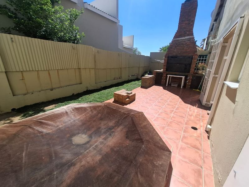 Rear courtyard featuring a built-in brick braai, tiled patio area, and a swimming pool with a cover, enclosed by a corrugated metal fence.
