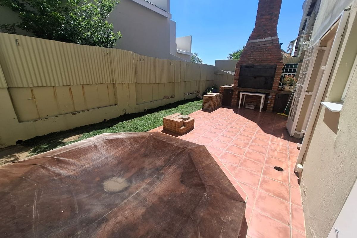 Rear courtyard featuring a built-in brick braai, tiled patio area, and a swimming pool with a cover, enclosed by a corrugated metal fence.