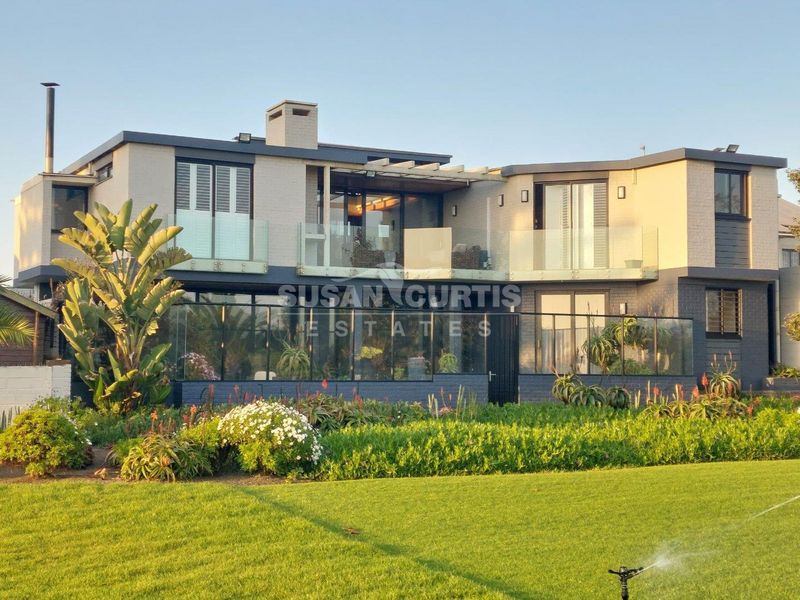 Rear elevation of a modern two-story residence featuring glass balustrades, a chimney, and a well-maintained landscaped garden with an integrated irrigation system.