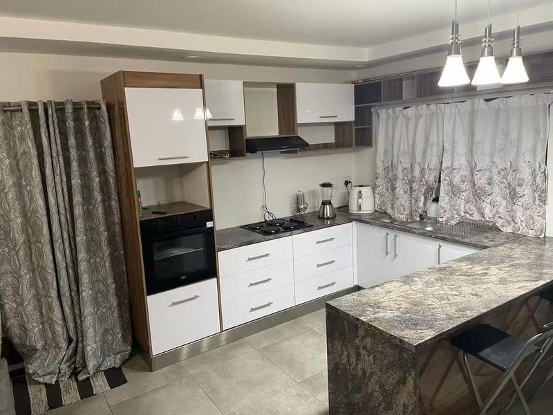Modern kitchen featuring white and wood-grain cabinetry, dark stone-look countertops, a breakfast bar, built-in oven, gas hob, and tiled flooring.