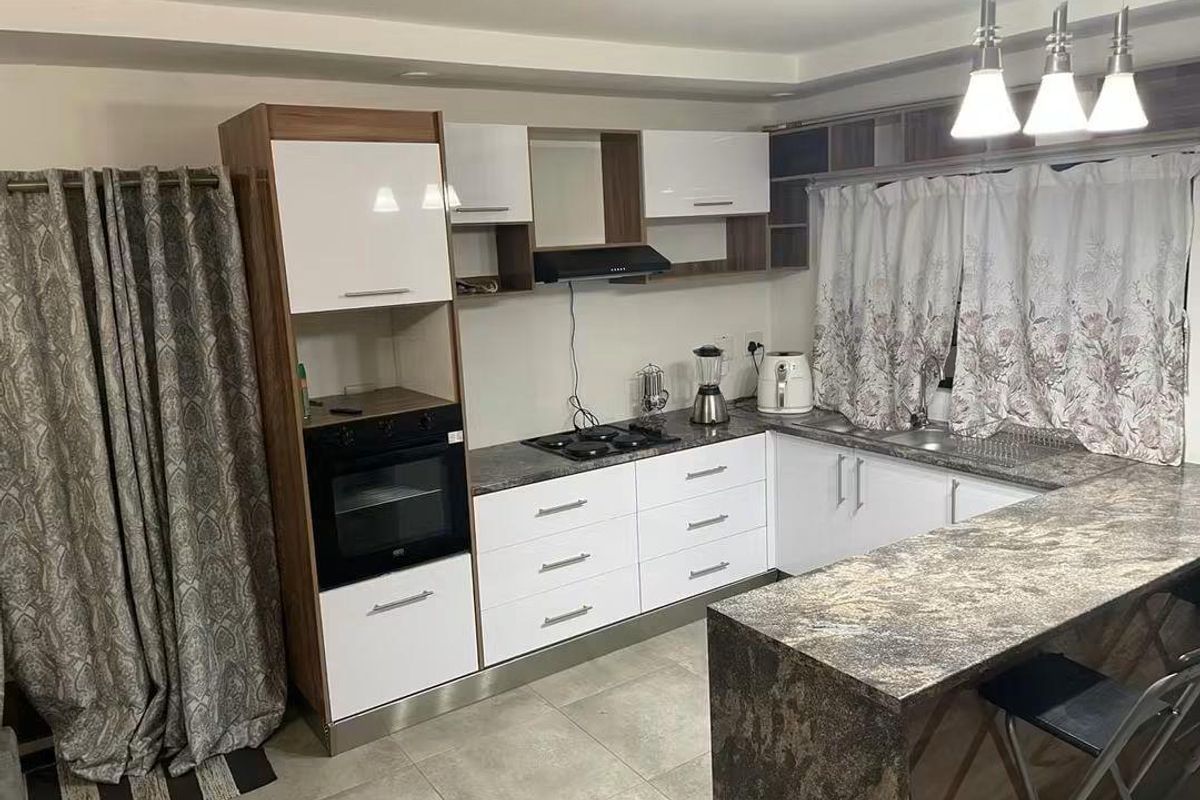 Modern kitchen featuring white and wood-grain cabinetry, dark stone-look countertops, a breakfast bar, built-in oven, gas hob, and tiled flooring.
