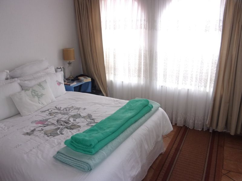 A bedroom featuring tiled flooring and large windows with curtain rails, providing natural light.
