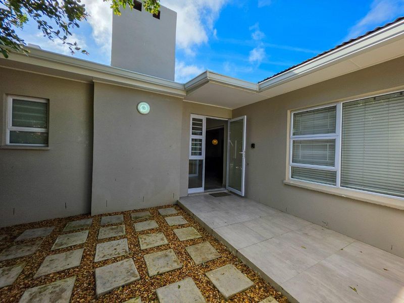 A well-maintained rear exterior area featuring a tiled patio, paver walkway, and a prominent chimney structure.