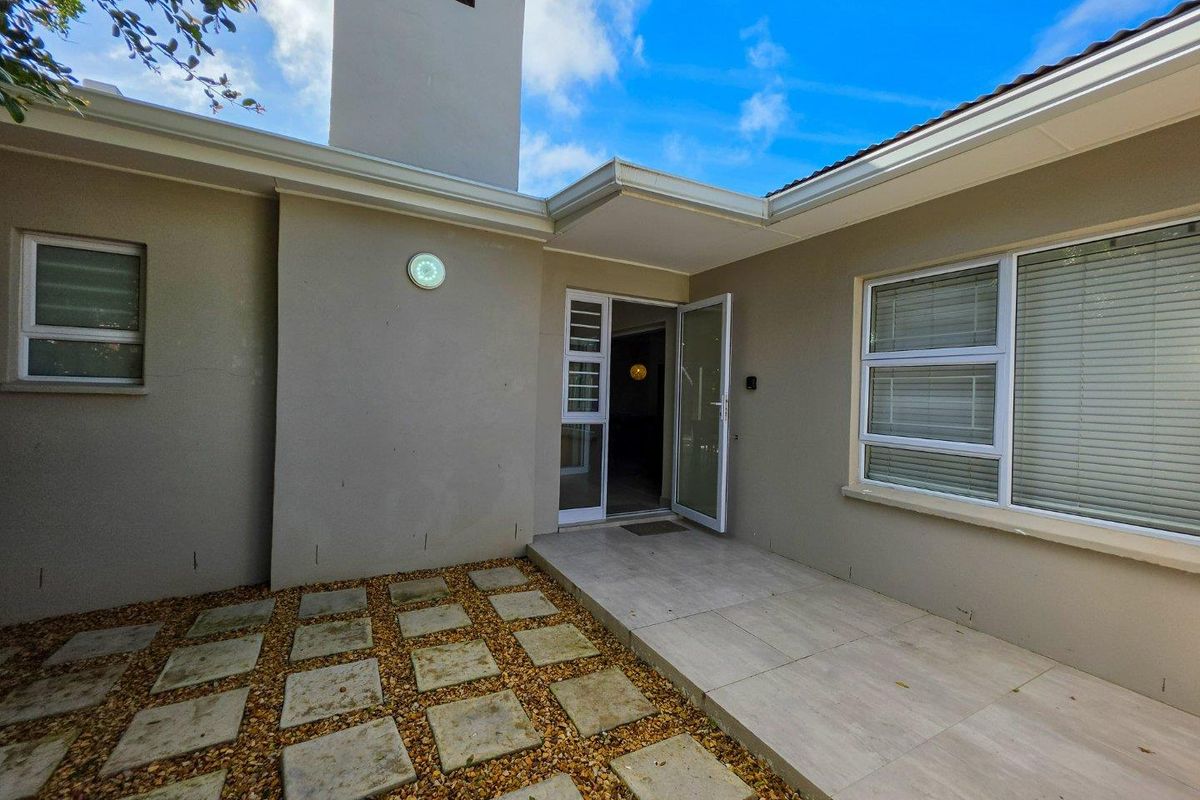 A well-maintained rear exterior area featuring a tiled patio, paver walkway, and a prominent chimney structure.