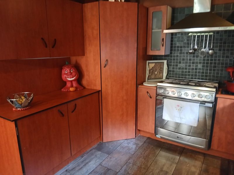 A functional kitchen featuring warm-toned wooden cabinetry, a stainless steel oven with an extractor fan, and a dark tiled backsplash.