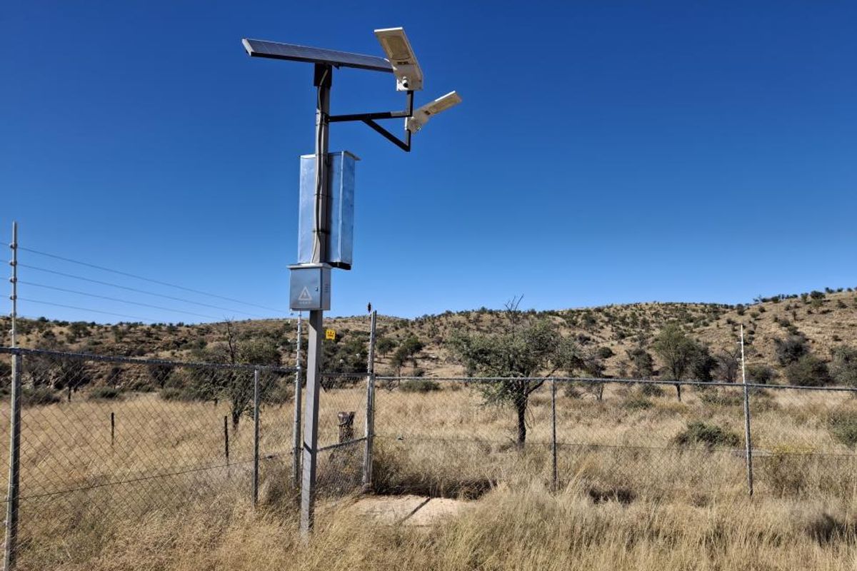 A security installation featuring solar-powered lighting and cameras mounted on a pole, situated within a fenced perimeter on the small holding.