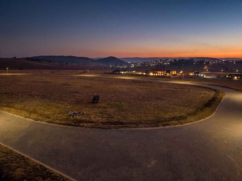 Aerial view of a vacant residential plot at dusk, featuring paved road access and established street lighting in a developing estate.