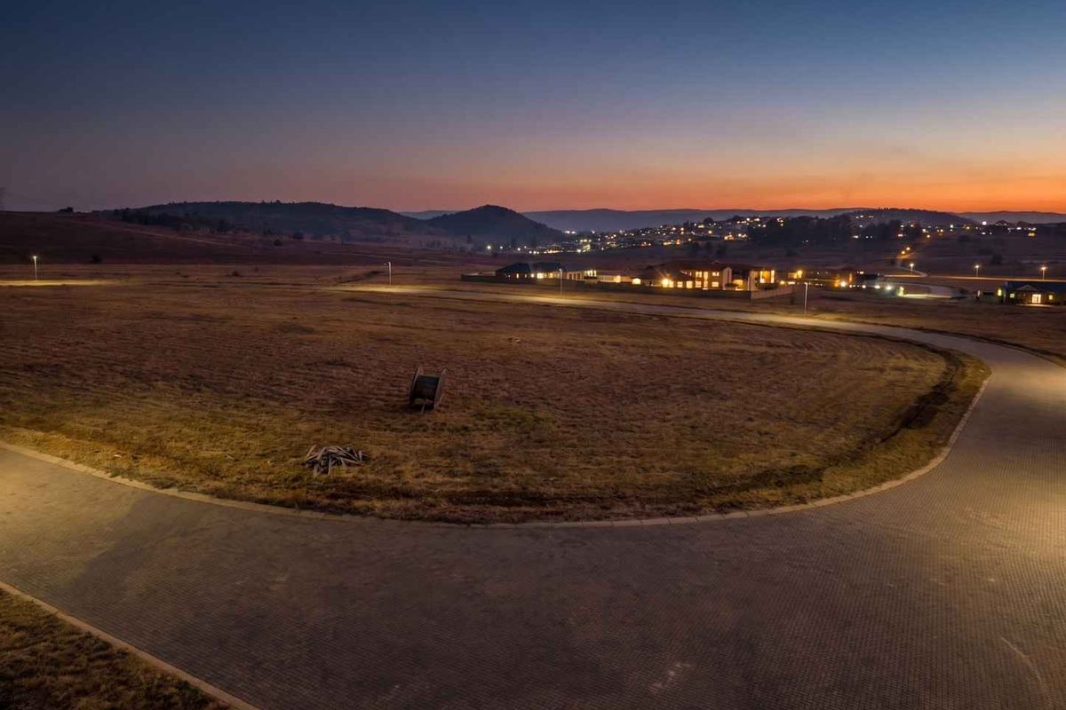 Aerial view of a vacant residential plot at dusk, featuring paved road access and established street lighting in a developing estate.