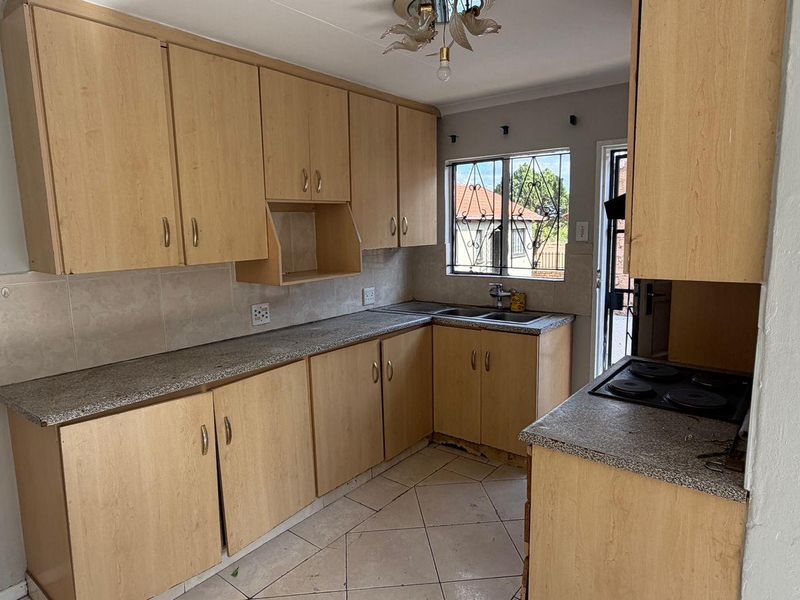 A functional kitchen featuring laminate cabinetry, granite-look countertops, a built-in hob, and tiled flooring, offering a practical layout ready for modernization.