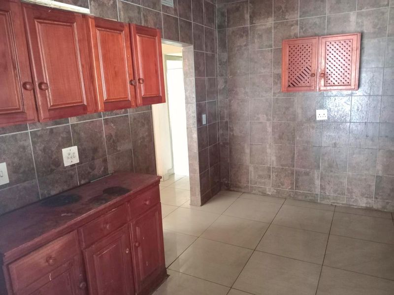 A dated kitchen featuring wooden cabinetry, full-height wall tiling, and tiled flooring, offering a blank canvas for potential renovation and modernization.