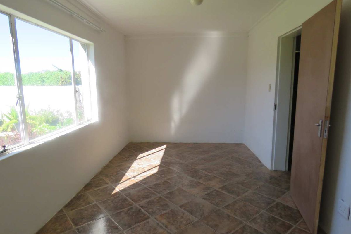 A bright, empty bedroom featuring tiled flooring, large windows allowing natural light, and a standard interior door.