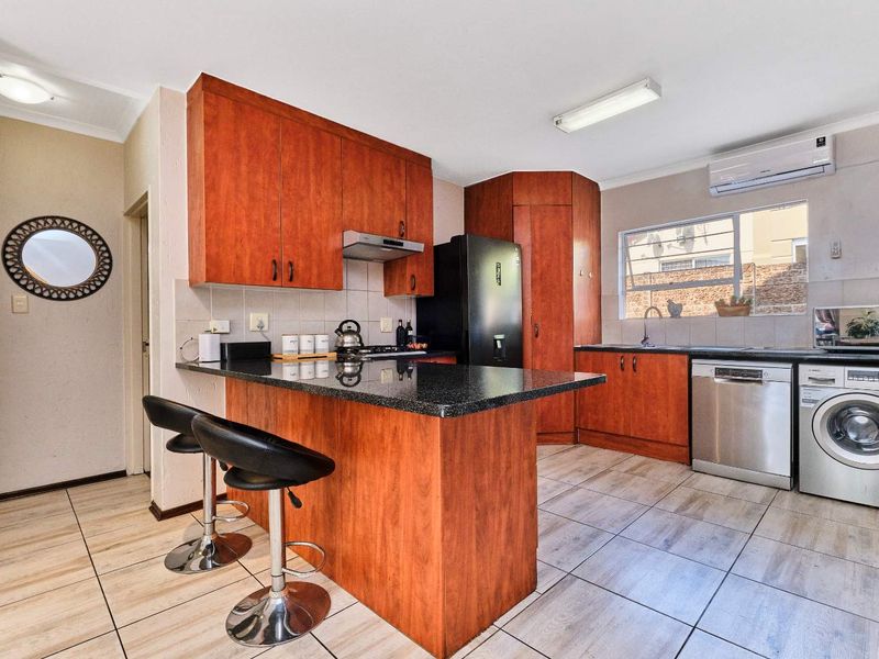 A functional kitchen featuring warm-toned wooden cabinetry, granite countertops, a breakfast bar, and integrated space for laundry appliances.
