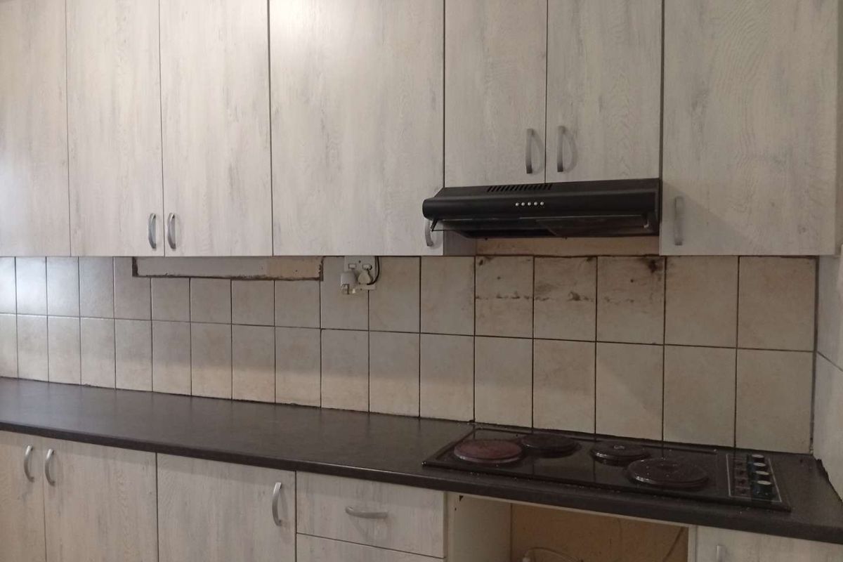 Kitchen area featuring light wood-grain cabinetry, dark countertops, and an electric hob. The space requires maintenance to the backsplash and cabinetry finish.