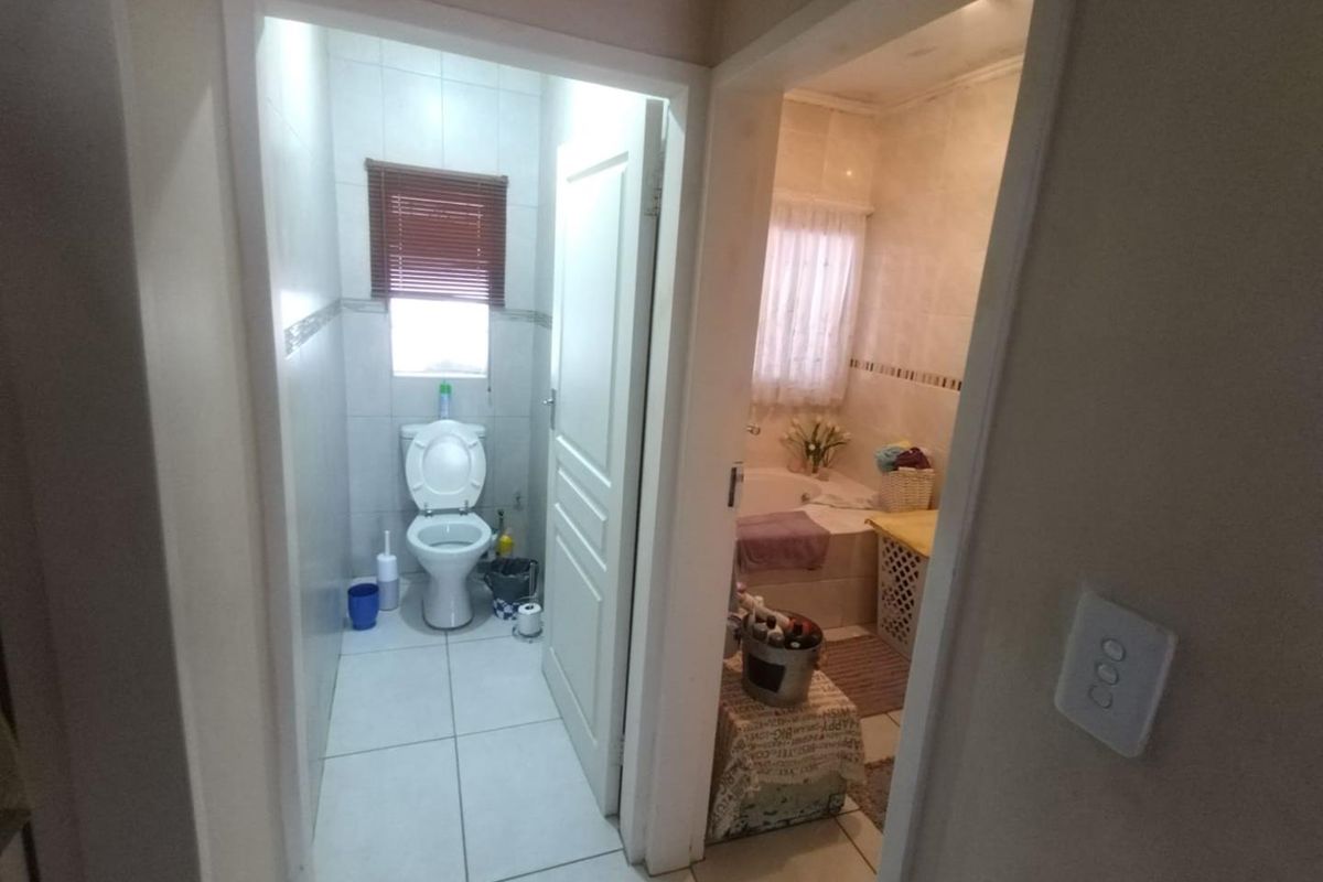 A functional bathroom layout featuring a separate toilet area and a bathtub, finished with neutral wall and floor tiles.