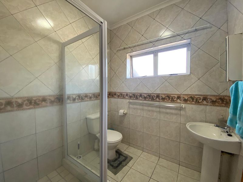 A functional bathroom featuring a shower enclosure, pedestal basin, and toilet, finished with neutral wall and floor tiling.