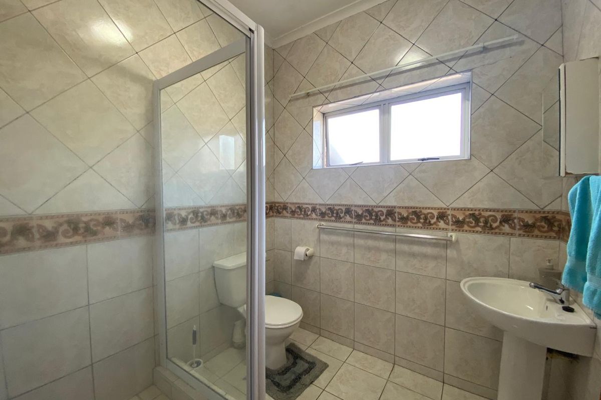 A functional bathroom featuring a shower enclosure, pedestal basin, and toilet, finished with neutral wall and floor tiling.