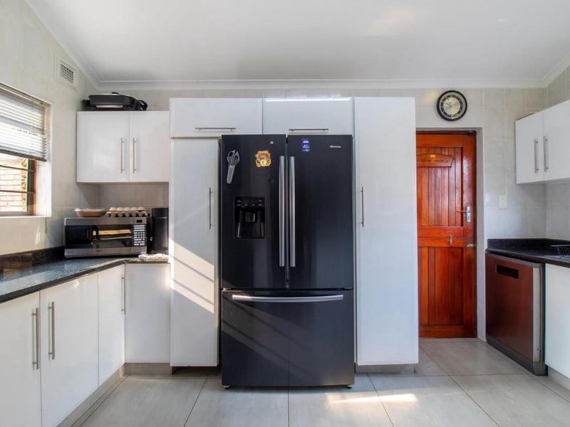 A functional kitchen featuring white cabinetry, dark granite countertops, tiled flooring, and a tiled backsplash, providing a clean and practical workspace.