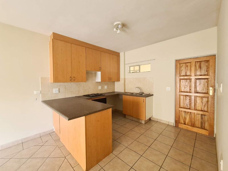 A functional kitchen featuring laminate cabinetry, built-in oven and hob, tiled flooring, and a tiled backsplash, presented in a clean, empty state.