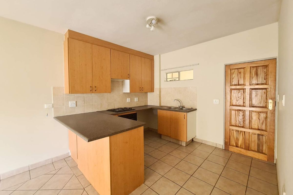 A functional kitchen featuring laminate cabinetry, built-in oven and hob, tiled flooring, and a tiled backsplash, presented in a clean, empty state.