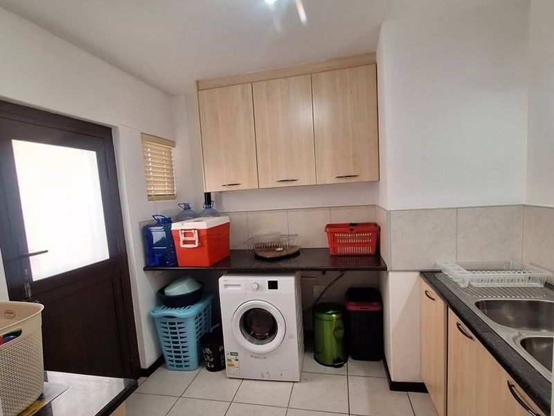 Functional laundry room featuring built-in light wood cabinetry, granite countertops, a stainless steel sink, and tiled flooring with space for a washing machine.