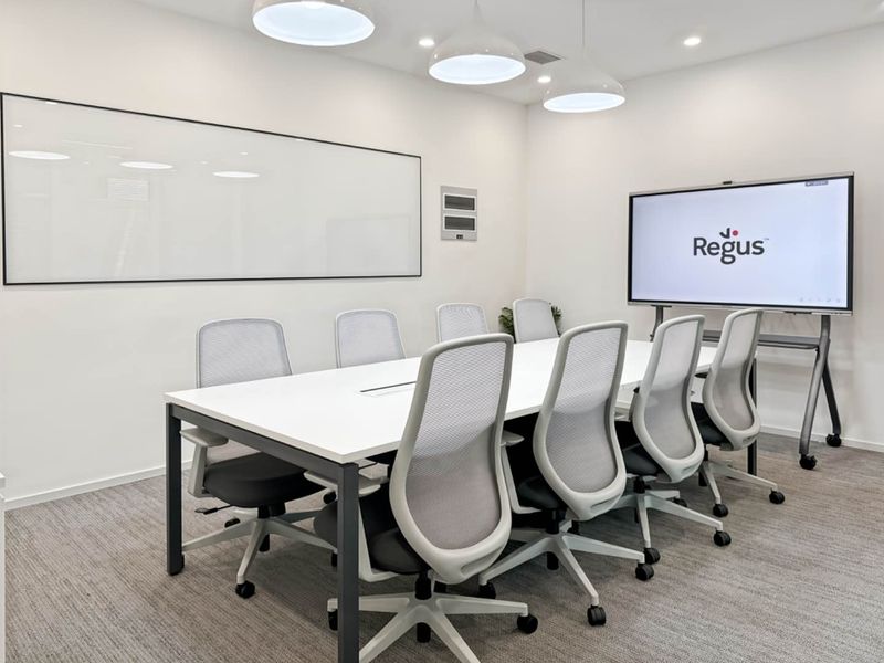 A modern, well-lit professional meeting room featuring a large conference table, wall-mounted whiteboard, and integrated presentation screen in a clean, corporate office environment.