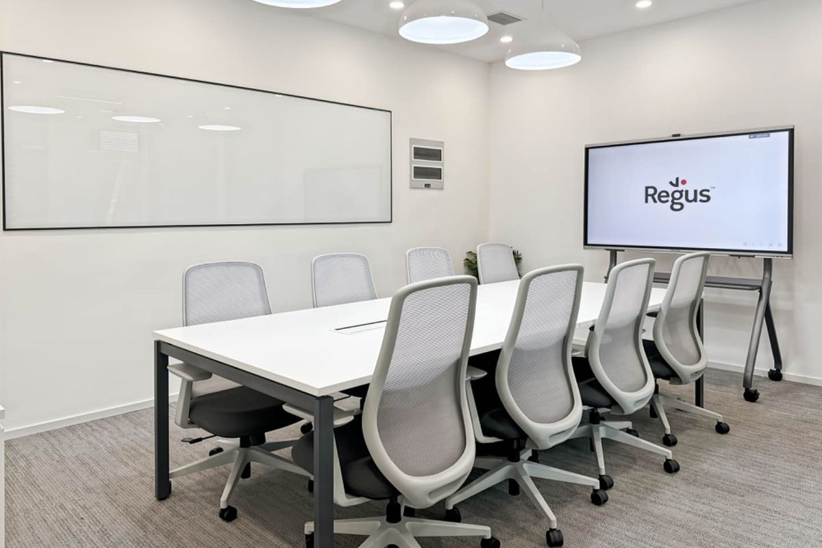 A modern, well-lit professional meeting room featuring a large conference table, wall-mounted whiteboard, and integrated presentation screen in a clean, corporate office environment.