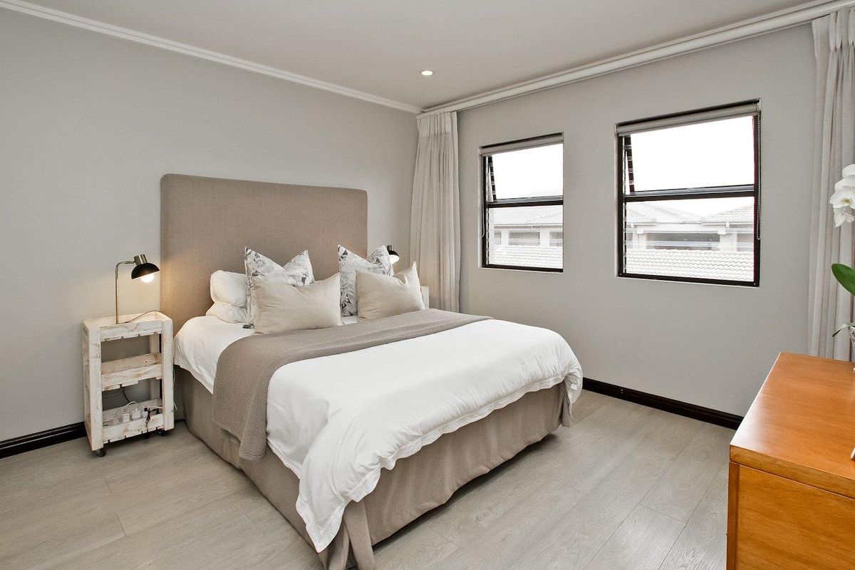 A well-maintained bedroom featuring light-toned laminate flooring, neutral wall finishes, and dual windows with integrated curtain tracks and recessed ceiling lighting.