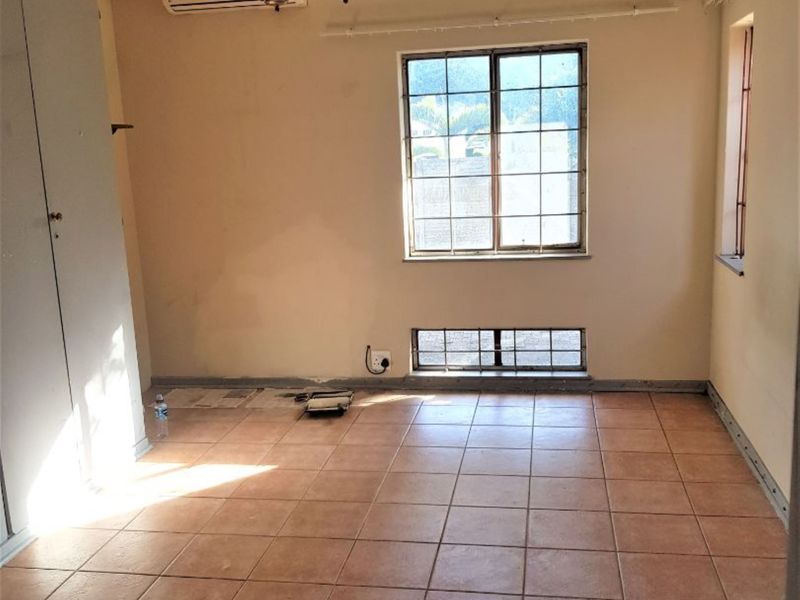 An empty bedroom featuring tiled flooring, built-in cupboards, a split-system air conditioner, and security bars on the windows.