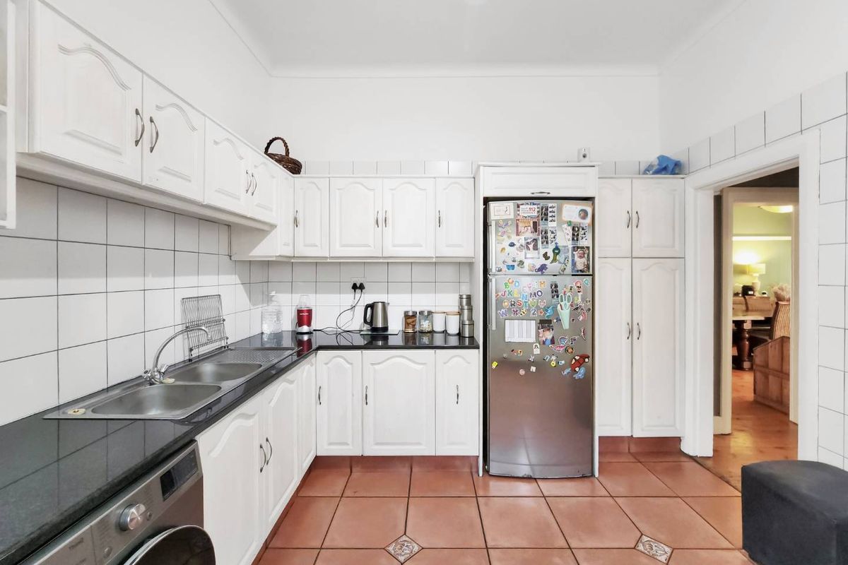 A functional kitchen featuring white cabinetry, black granite countertops, a double stainless steel sink, and terracotta floor tiles with a built-in pantry.