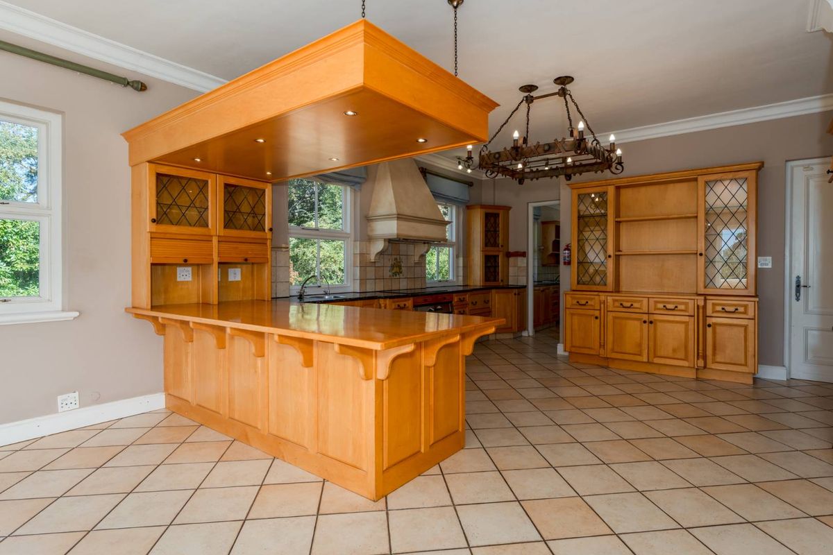 Spacious kitchen featuring extensive light wood cabinetry, a large central island with overhead lighting, tiled flooring, and a classic range hood.