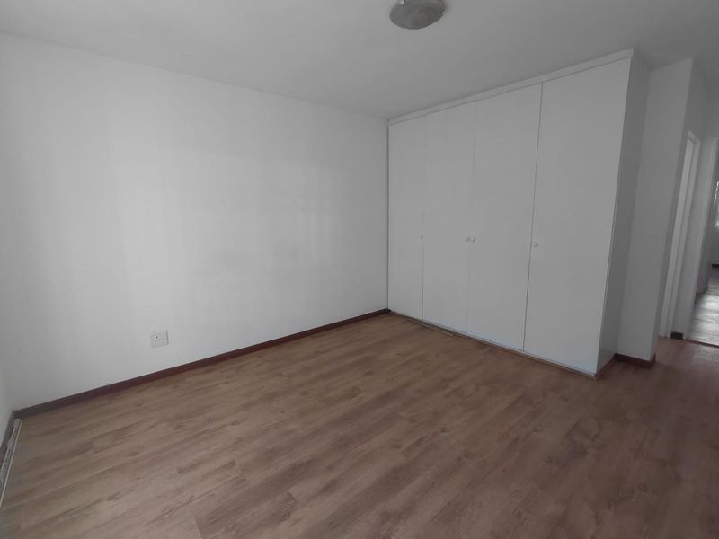A clean, empty bedroom featuring light wood-look laminate flooring and white built-in cupboards, offering a neutral canvas for personalization.